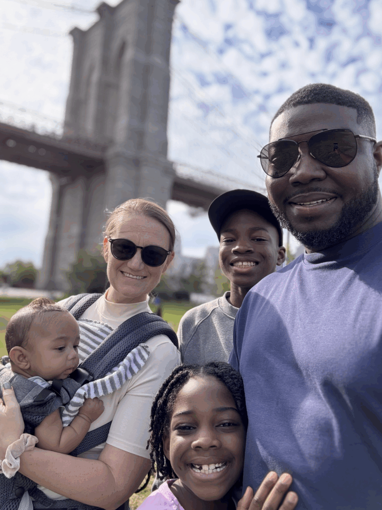A family of five smiles in front of the Brooklyn Bridge on a sunny day, symbolizing unity, hope, and legacy building.
